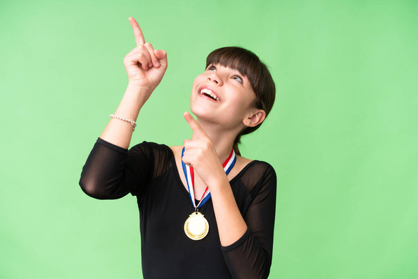 Petite fille caucasienne avec des médailles sur fond isolé pointant avec l'index une excellente idée - Photo, image