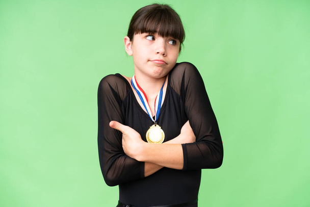 Petite fille caucasienne avec des médailles sur fond isolé faisant des doutes geste tout en soulevant les épaules - Photo, image