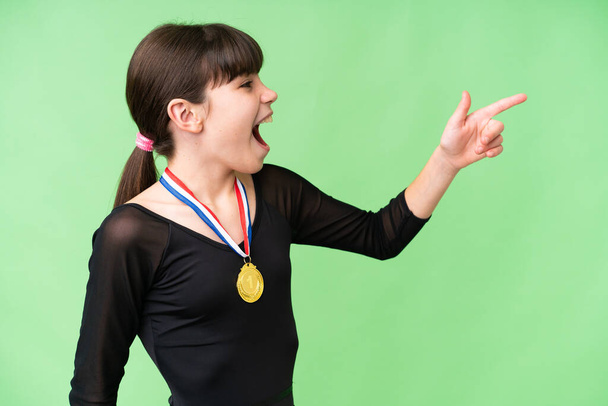 Petite fille caucasienne avec des médailles sur fond isolé pointant loin - Photo, image