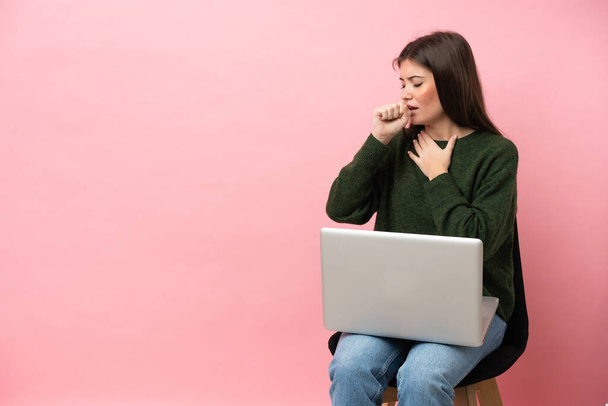 Молода біла жінка сидить на стільці з ноутбуком ізольовано на рожевому фоні страждає від кашлю і погано себе почуває
 - Фото, зображення