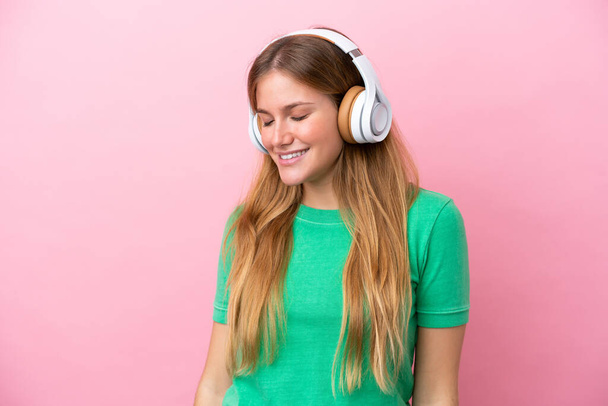Joven rubia aislada sobre fondo rosa escuchando música - Foto, Imagen