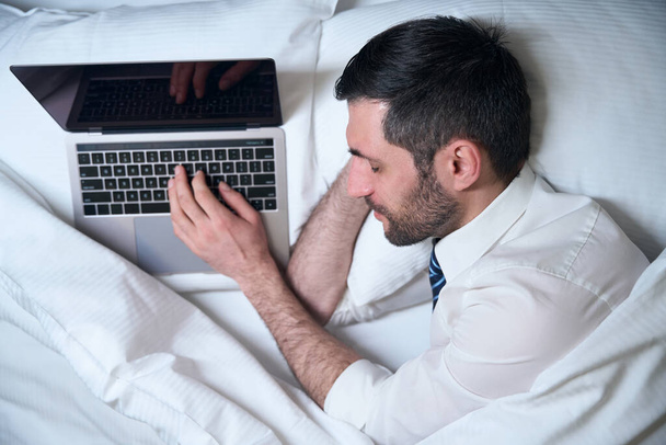 Tired male fell asleep, without undressing, at work on the laptop, he settled down on a comfortable bed - Foto, Imagen