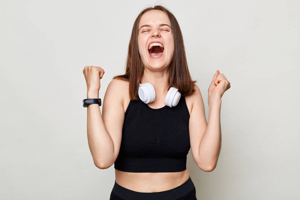 Extremely happy woman wearing black top standing isolated over white background clenched fists screaming with happiness celebrating her success. - Фото, зображення