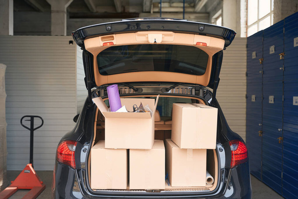 Cardboard big boxes with things are standing in the open trunk of a hatchback in a storage warehouse - Photo, image