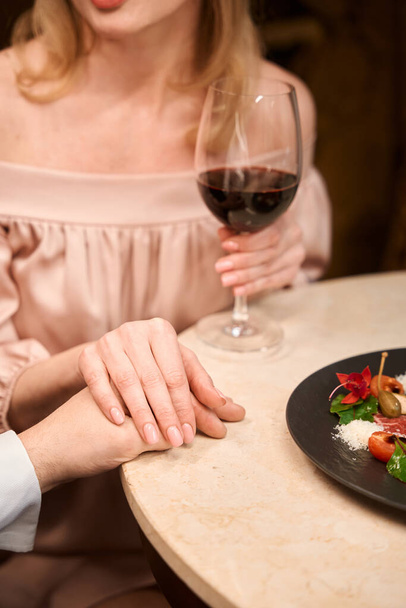Close up of lovely couple holding each holding each others hands and having romantic dinner at table in the restaurant - Foto, Imagen