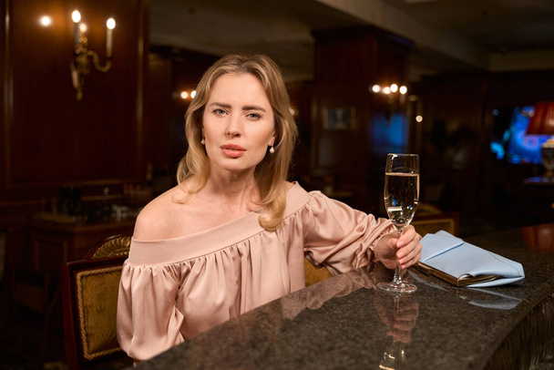 Adult woman in evening dress chilling with glass of wine and waiting for colleague at the table in bar - Foto, imagen