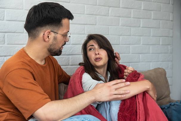 Couple at home. Handsome young man is calming his upset crying wife while holding her shoulders and apologizes. People, relationship difficulties, conflict and family concept - Foto, immagini