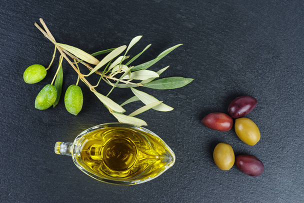 Delicious olive oil, black and green olives with leaves, over black stone slate background - Фото, изображение