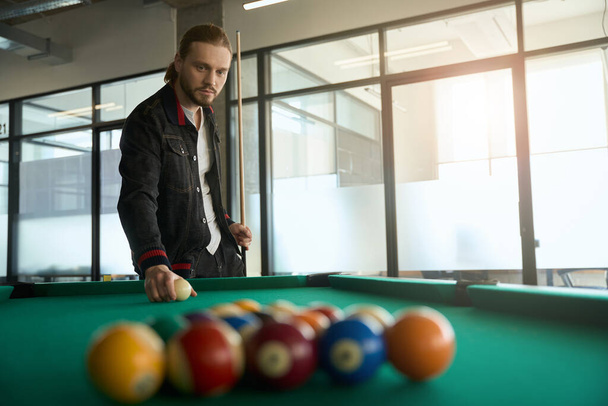 Young billiard player putting game ball on pool table and holding cue indoors - Foto, Imagem
