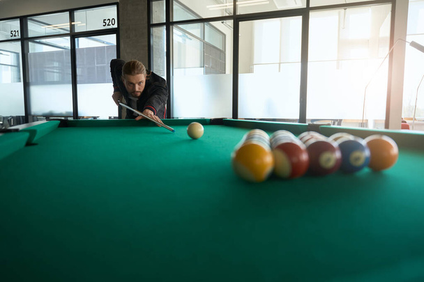 Concentrated billiard player in fancy clothes preparing to shot billiard ball with cue indoors - Fotografie, Obrázek