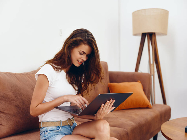 Kobieta freelancer siedzi na kanapie z laptopem piękny uśmiech, nowoczesne stylowe wnętrze skandynawskiego stylu życia, przestrzeń do kopiowania. Wysokiej jakości zdjęcie - Zdjęcie, obraz