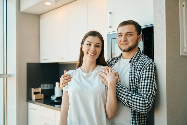 Happy young man tenderly hugs his wife by the shoulders, guys in comfortable home clothes - Фото, зображення