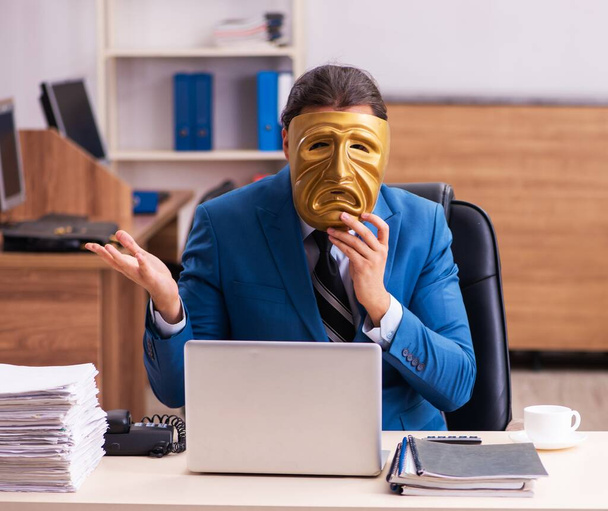 Egy fiatal alkalmazott szomorú maszkot visel az irodában. - Fotó, kép