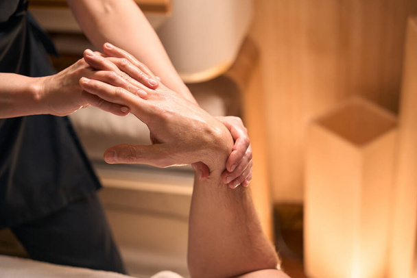 Nitelikli beyaz masaj terapistinin yetişkin bir adamın parmaklarını uzatırken çekilmiş fotoğrafı. - Fotoğraf, Görsel