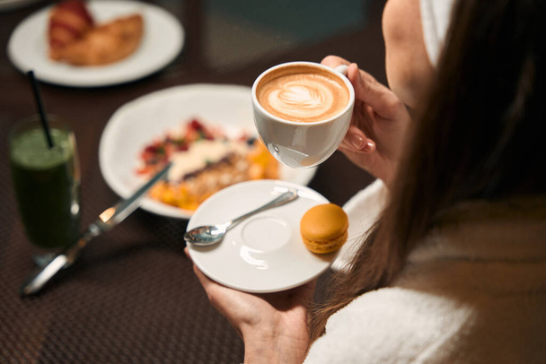 彼女の手にコーヒーのカップと朝食テーブルに座ってバスローブの女性の作物写真 - 写真・画像