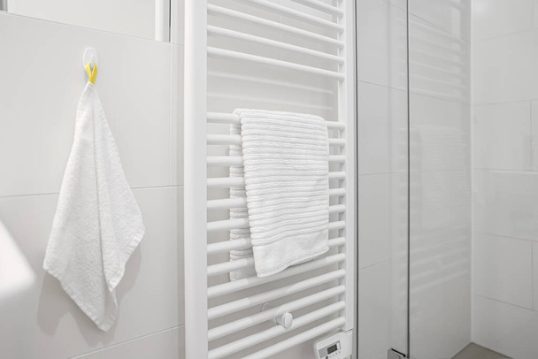 Verwarmde handdoekhouder in de buurt van lichte muur in de badkamer - Foto, afbeelding