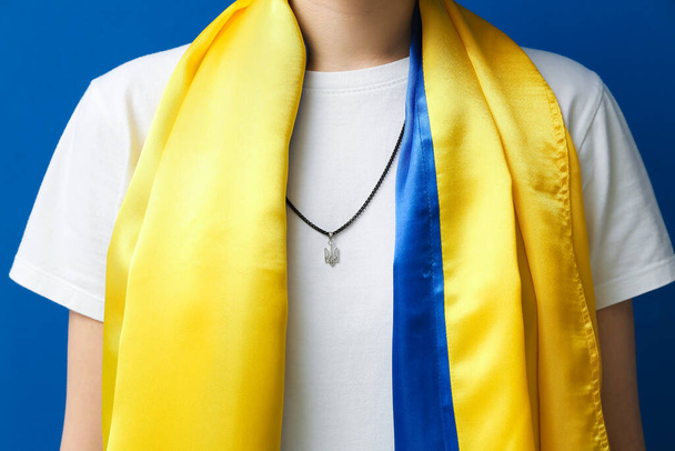 Woman in chain with Ukrainian coat of arms and flag on blue background, closeup - Fotó, kép