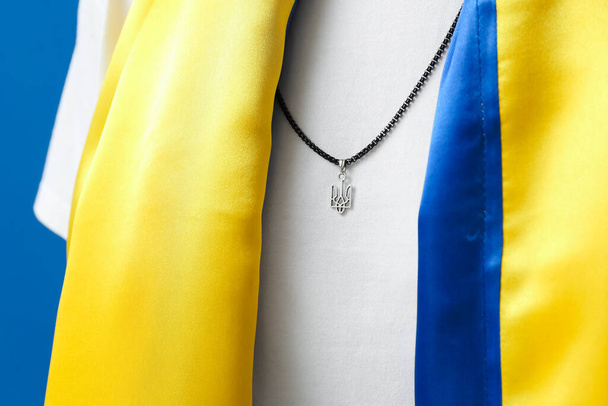 Mujer en cadena con escudo de armas ucraniano y bandera sobre fondo azul, primer plano - Foto, imagen