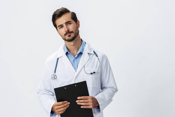 Man arts in witte jas met stethoscoop en record map en patiëntenkaart ongelukkig boos op witte geïsoleerde achtergrond, kopieer ruimte, ruimte voor tekst, gezondheid. Hoge kwaliteit foto - Foto, afbeelding