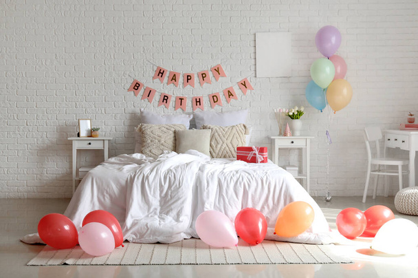 Interior of bedroom decorated for birthday with balloons, gift box and garland - Фото, зображення