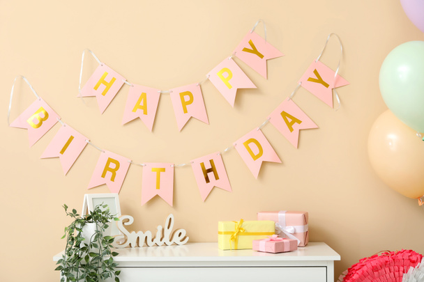 Cofre de cajones con cajas de regalo y guirnalda cerca de la pared beige en la sala de estar decorada para el cumpleaños - Foto, imagen