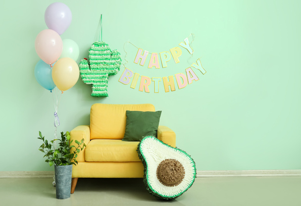 Keltainen nojatuoli, piñatas, ilmapalloja ja Garland lähellä vihreää seinää olohuoneessa koristeltu syntymäpäivä - Valokuva, kuva