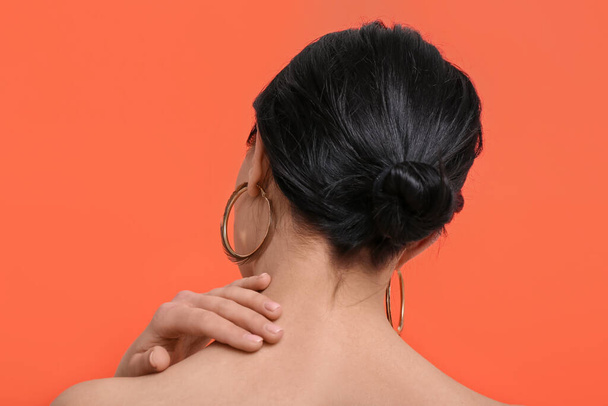 Beautiful young woman wearing stylish earrings near orange wall, back view - Фото, зображення