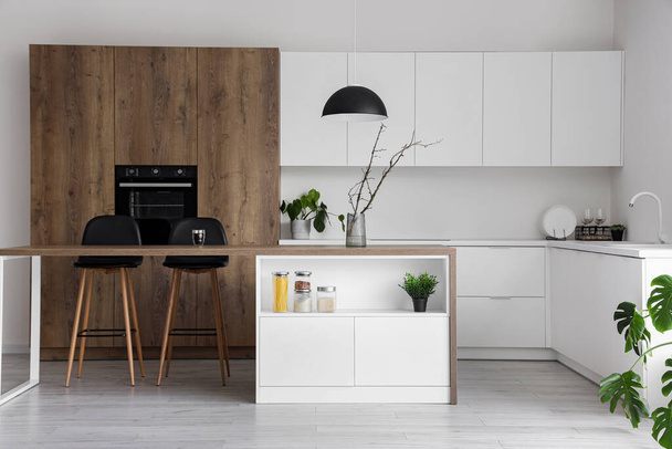 Interior of modern kitchen with island, built-in oven and white counters - Foto, afbeelding