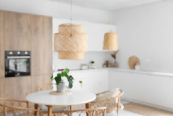 Interieur van lichte keuken met ingebouwde oven, tafel, stoelen en witte balies, wazig uitzicht - Foto, afbeelding