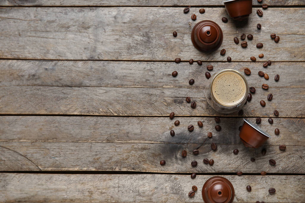 Стакан вкусного кофе, стручки и бобы на деревянном столе - Фото, изображение