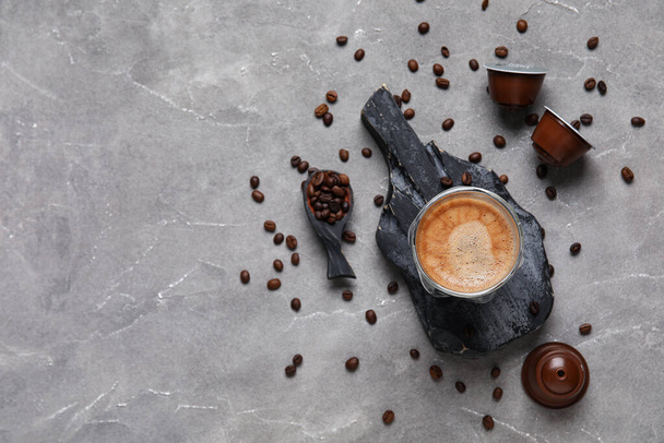 Slate board with cup of delicious espresso, beans and capsules on grey grunge table - Photo, Image