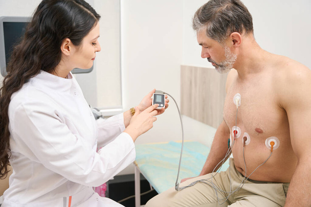 Médico joven que presenta indicaciones de trabajo del sistema cardiovascular al hombre en el hospital - Foto, imagen