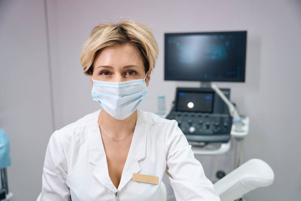Foto di una ginecologa donna che lavora con una maschera medica sullo sfondo di una macchina ad ultrasuoni - Foto, immagini