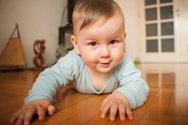 Portrait of cute happy smiling baby boy crawls on the home floor and looking at camera. Joy and happiness concept. Love and family emotion - Foto, Bild