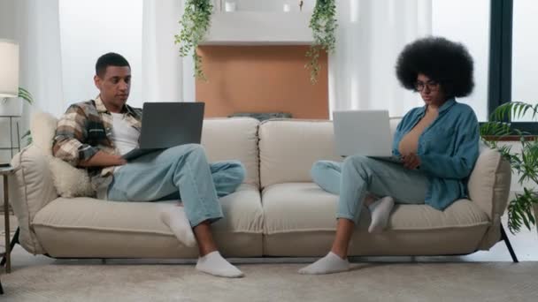 アフリカ系アメリカ人のカップル技術ビデオゲーム中毒家族と2台のラップトップはソファの上でオンラインでプレイホーム女性はソファの上でコンピュータでフリーランスと一緒に働いているラップトップの男と仕事は無視 - 映像、動画