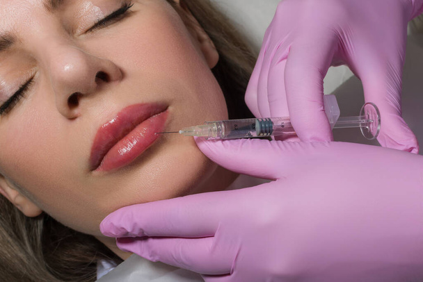 Close up portrait of woman getting botox cosmetic injection in the lips. Beautiful woman gets botox injection in her face. Adult girl gets cosmetic injection of botox in a clinic. Beauty treatments - Foto, afbeelding