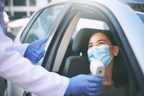 Böyle normal bir sıcaklık görmeyi seviyorum. Maskeli genç bir kadın arabasında otururken bir doktor ateşini ölçüyor. - Fotoğraf, Görsel