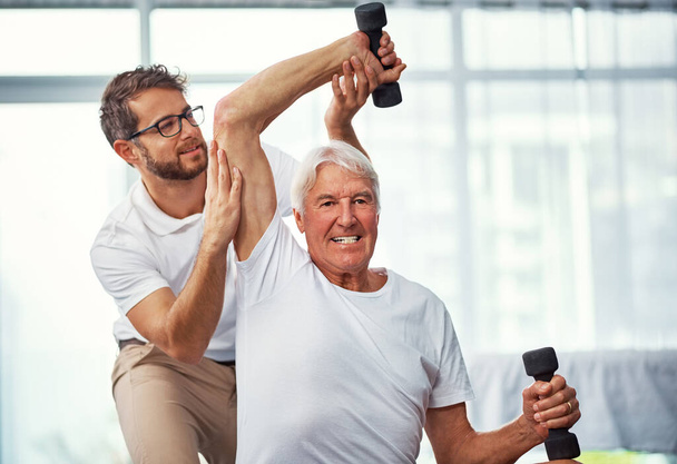 Ihm auf dem Weg der Besserung zu helfen. ein älterer Mann arbeitet mit einem männlichen Physiotherapeuten an seiner Genesung - Foto, Bild