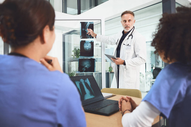Se réunir pour une autre pratique collaborative. un médecin mature analysant les rayons X avec ses collègues lors d'une réunion dans un hôpital - Photo, image