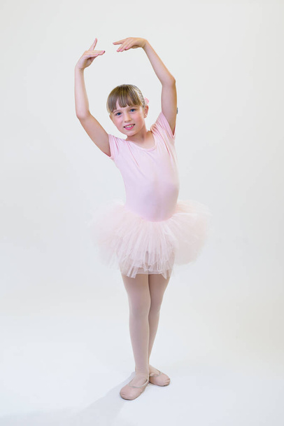 Little ballerina dancer in a pink tutu academy student posing on white background. - Фото, зображення