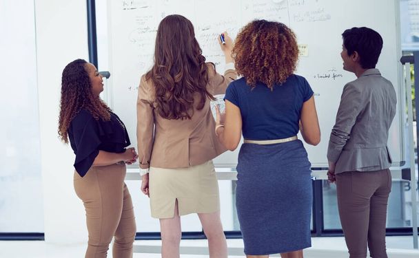 Gather around. Rearview shot of a group of businesswomen working on a whiteboard in the boardroom - Photo, Image