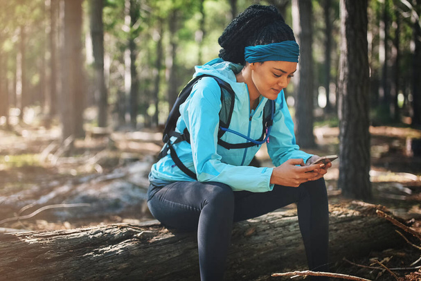 Champions are not bored. They are made. an athletic young woman sending a text while jogging in the woods - Foto, imagen