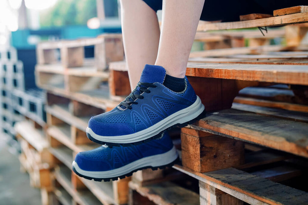 Photo of a woman sitting on old wood and wearing blue sports shoes, these shoes are often called sneakers - Photo, Image