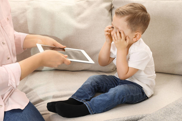 Internet addiction. Mother taking away tablet from her little son on sofa at home, closeup - Foto, imagen
