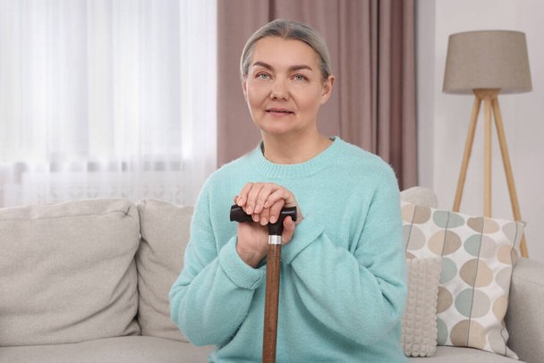 Senior woman with walking cane sitting on sofa at home - Zdjęcie, obraz