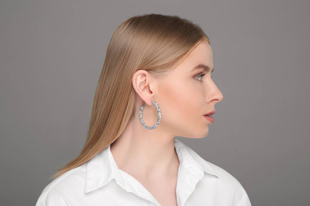 Beautiful young woman with elegant earrings on gray background - Zdjęcie, obraz