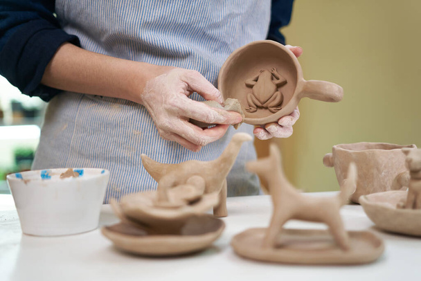 woman forming clay cup shape by hands, closeup in artistic studio. - 写真・画像