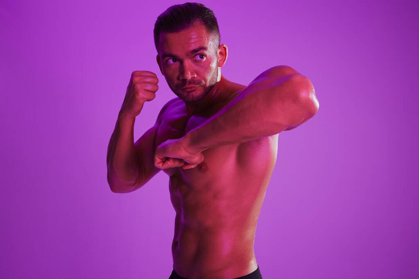 Człowiek kulturysta bokser mięśni trening z nagim tułowia. Reklama, sport, aktywny tryb życia, kolorowe fioletowe światło, rywalizacja, koncepcja wyzwania. - Tak. Wysokiej jakości zdjęcie - Zdjęcie, obraz