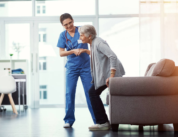 Dándole un poco de ayuda. Foto completa de una joven enfermera ayudando a su paciente mayor a levantarse de una silla en el hogar de ancianos - Foto, imagen