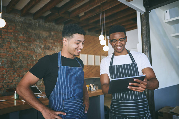 Intelligente come la gestione delle piccole imprese ottiene. due giovani uomini che usano un tablet digitale mentre lavorano in un caffè - Foto, immagini